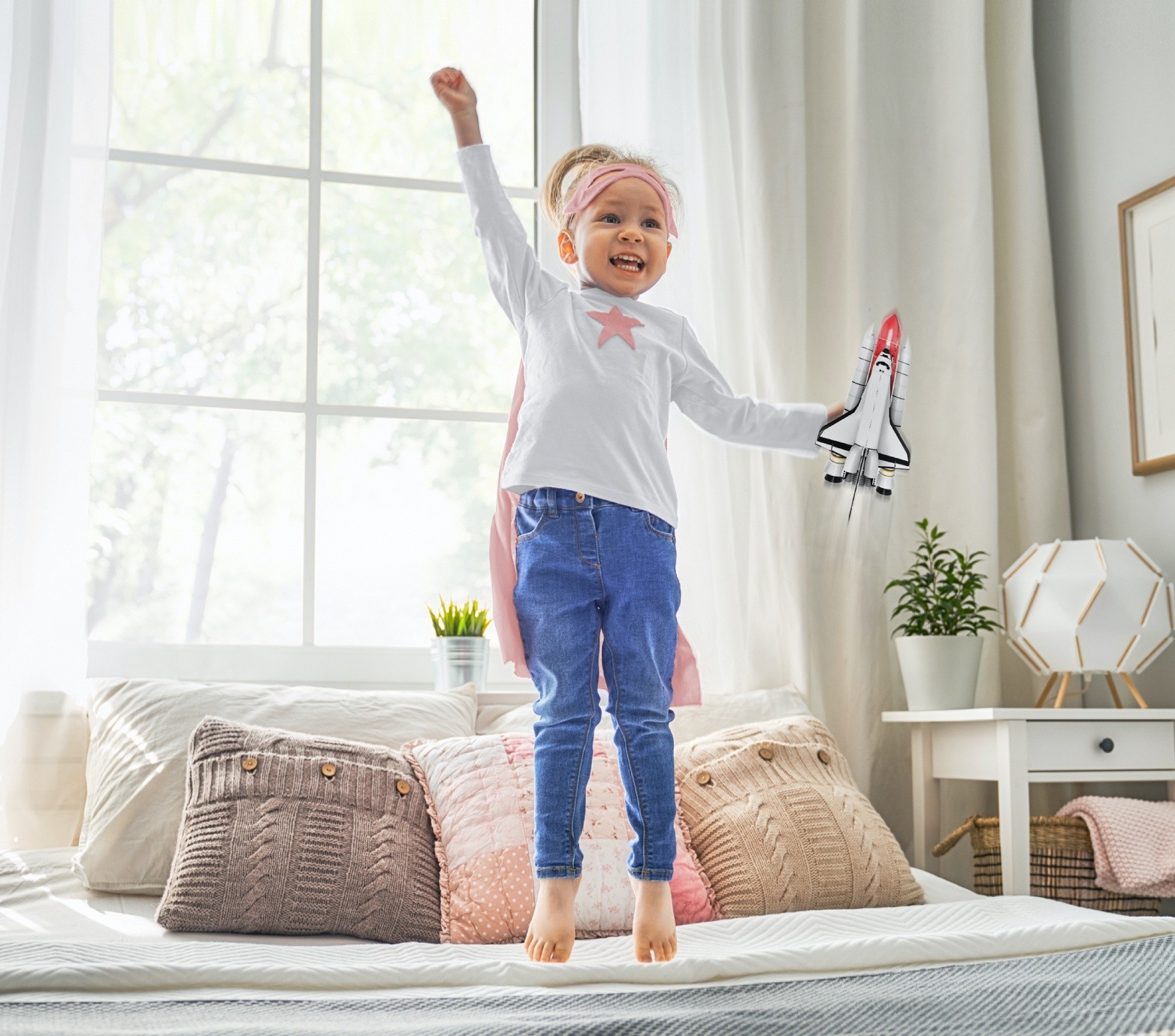 Little girl jumping on a bed with a rocketship in her hand