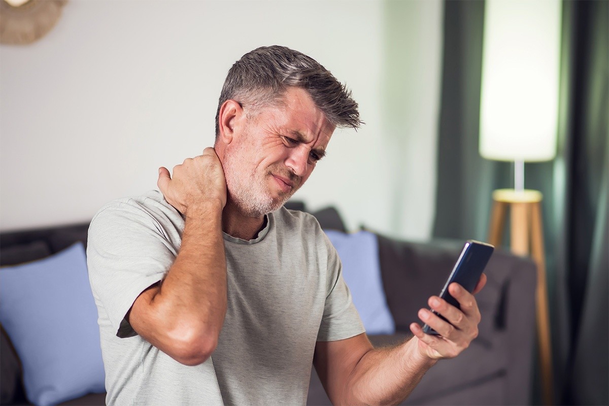 Man holding his phone in one hand and massaging the back of his neck with the other